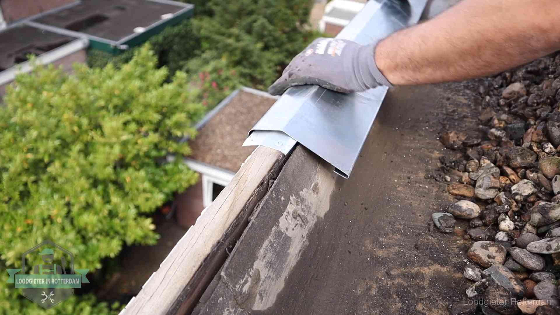 Daklekkage per wijk in Rotterdam Dakdekker plaatst een zinken deklijst op een dakrand met uitzicht over een woonwijk in Rotterdam