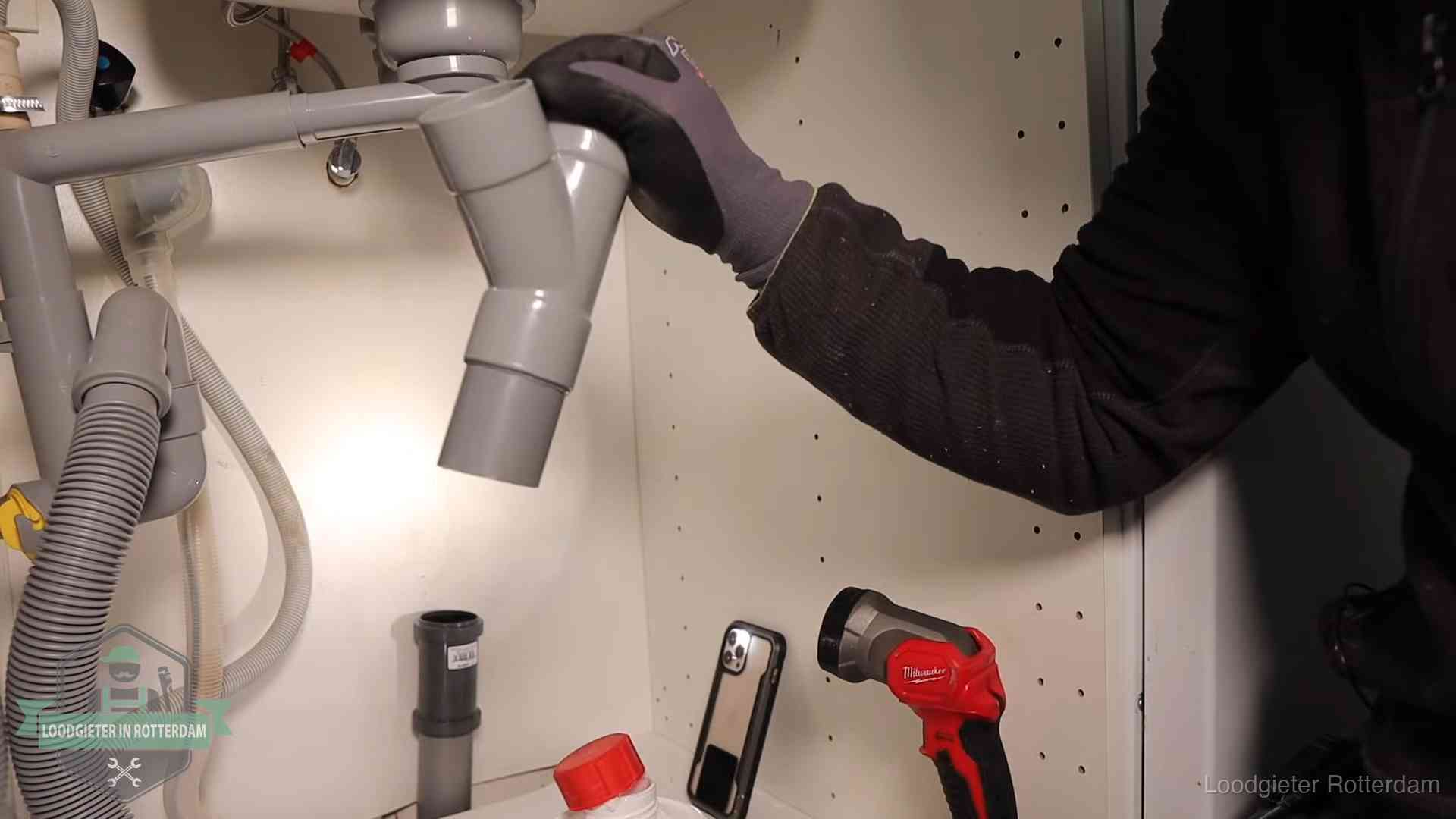 Loodgieter demonteert het sifon- en afvoerwerk onder een gootsteen in Rotterdam bij stankklachten