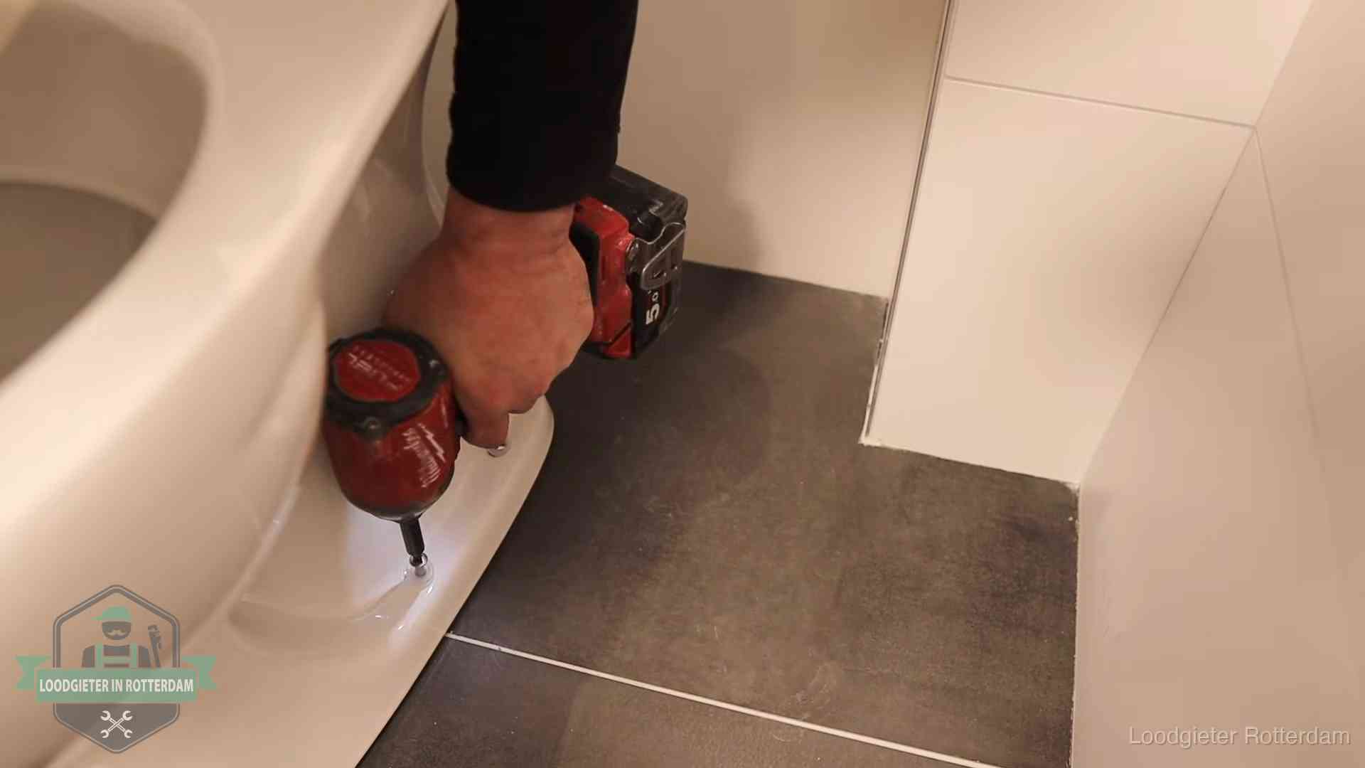 Loodgieter zet de voet van een wc-pot vast op de tegelvloer in Rotterdam